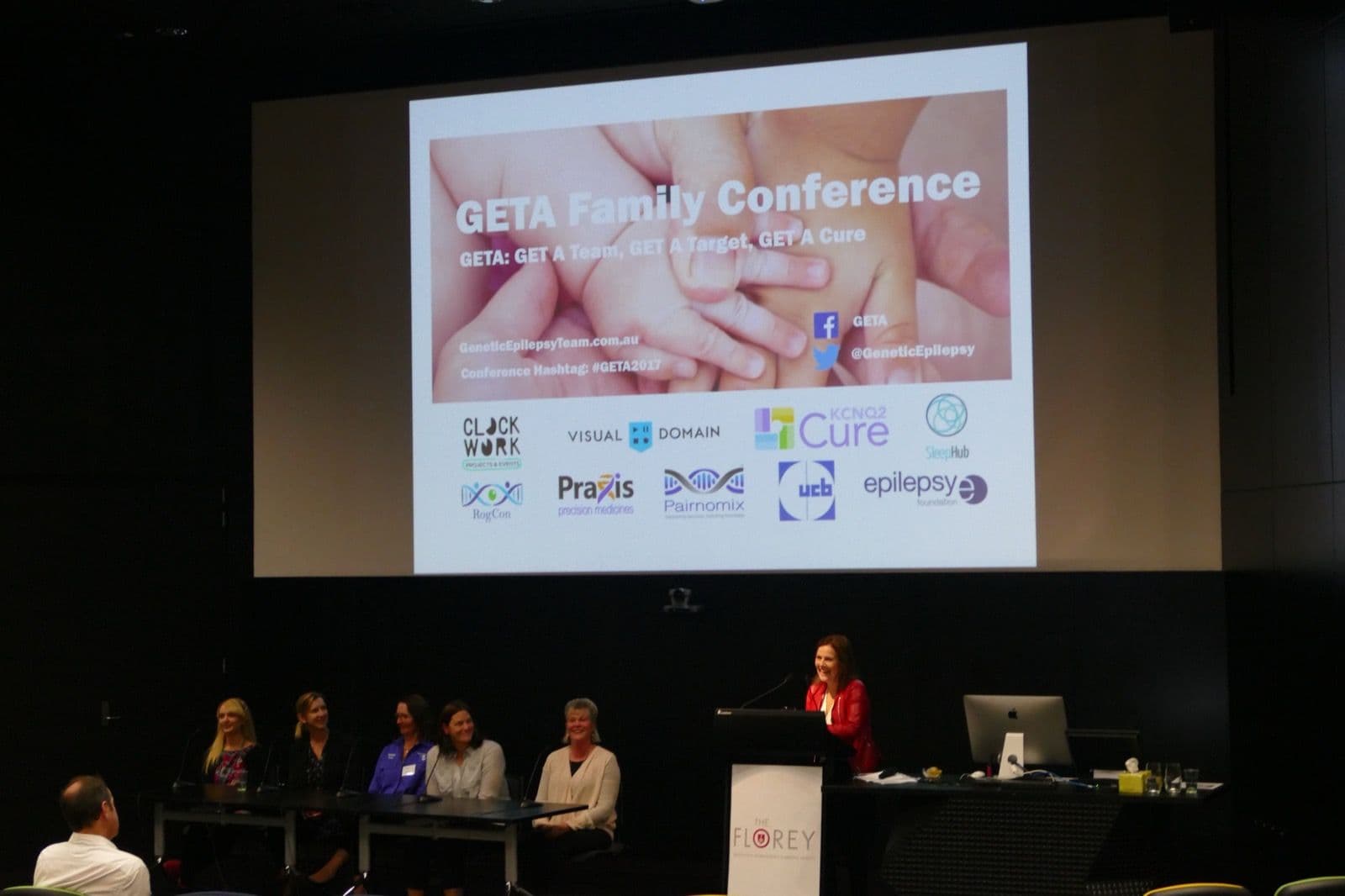 A speaker at the lectern and a panel of five seated on stage beneath the GETA Family Conference title slide